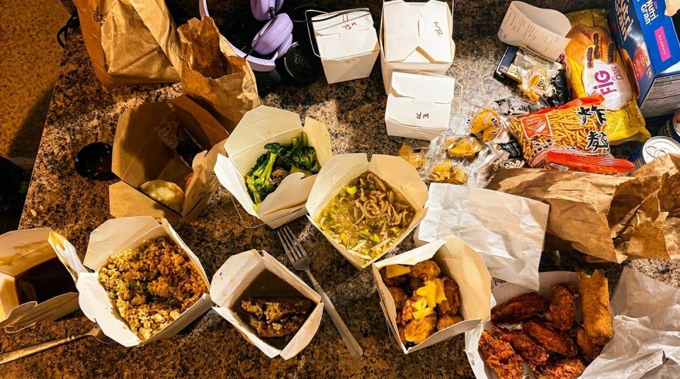 A messy table covered with various Chinese takeout containers, food, and packaging.