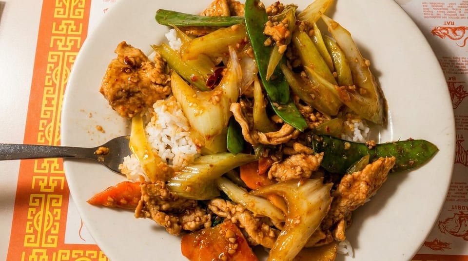 A close-up of a white plate filled with chicken stir-fry, rice, and vegetables.
